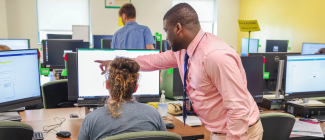 Advisor pointing at a computer monitor while assisting a student